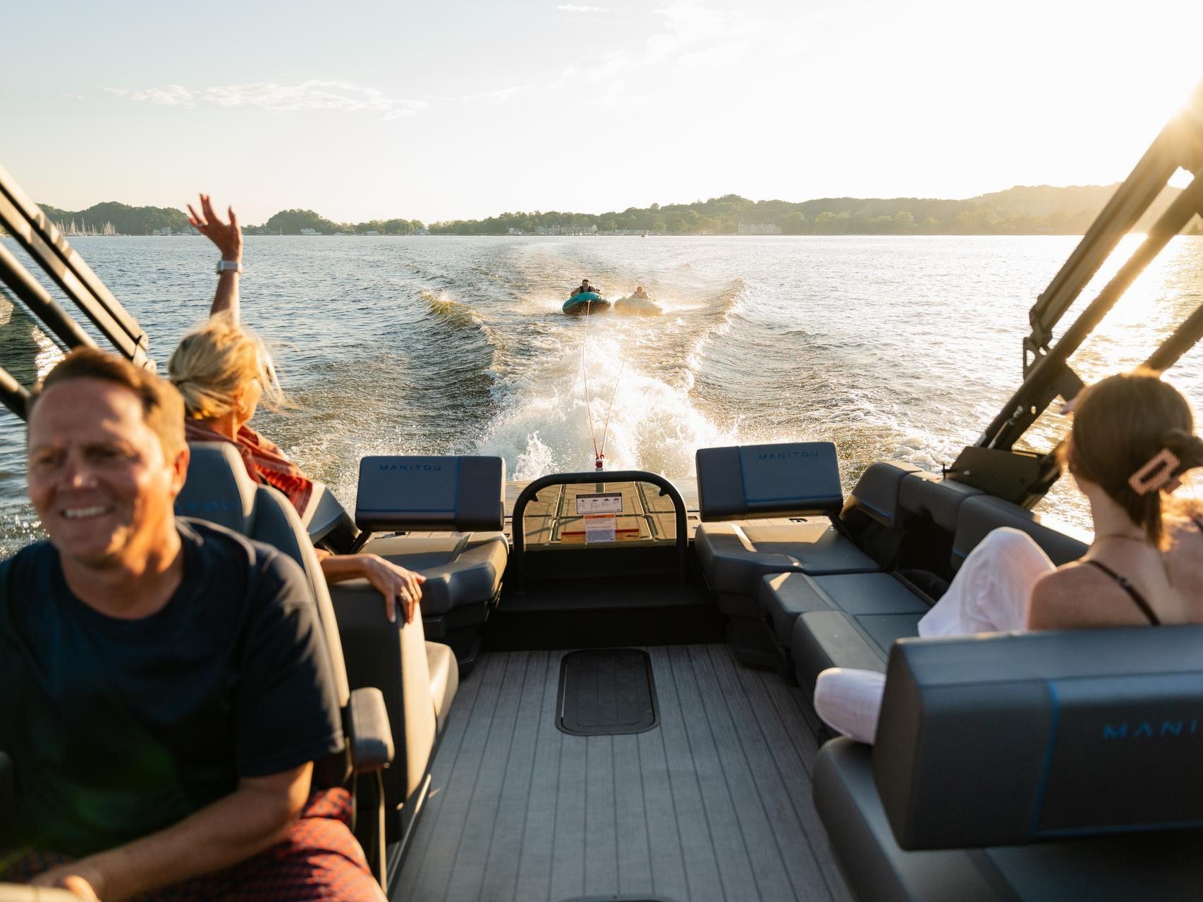 A family enjoying water sports behind a Manitou Explore 2025 pontoon boat